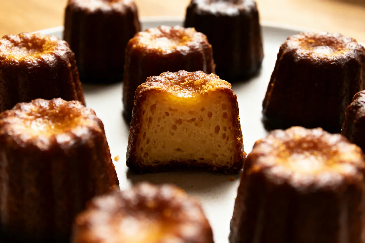 Des cannelés caramélisés sur une assiette, dont un est coupé en deux, révélant un intérieur moelleux.