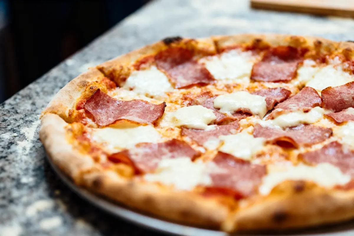 Pizza avec salami et fromage, posée sur une surface en marbre. Croûte dorée et garniture fondante.